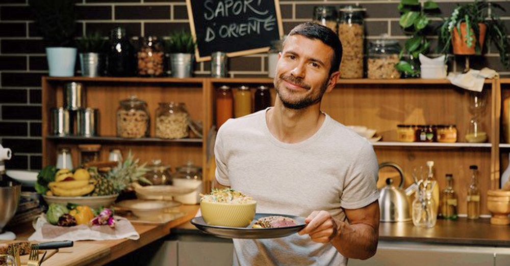 Davide Campagna in abiti da chef con piatto di pasta, logo Food Network sullo sfondo